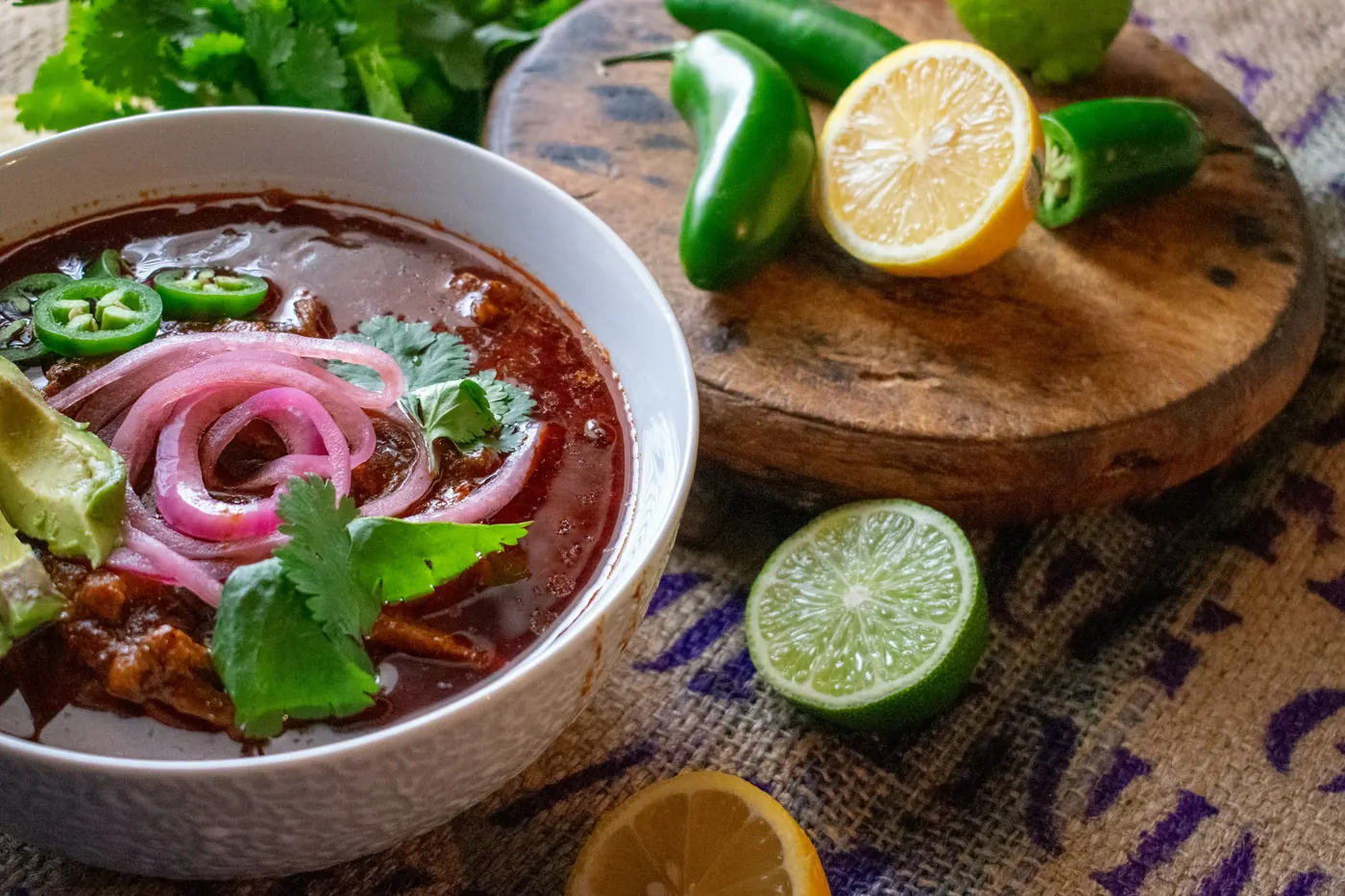 A bowl of red consome topped with pickled red onion, lime and jalapeno