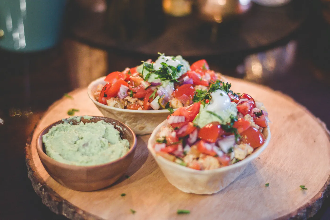 Wooden bowls of chopped pico de gallo and guacamole on a board