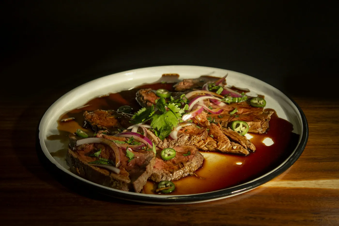 Sliced braised beef in a red chile sauce topped with pickled onion