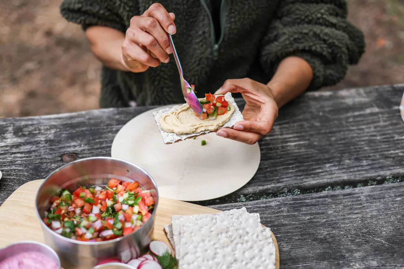Hands assembling a small taco with chopped tomato and onion