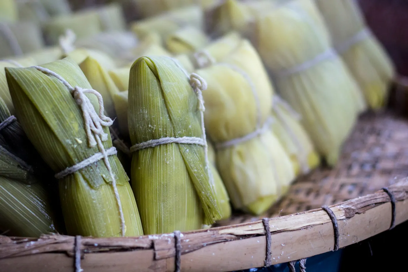 Bundles of wrapped tamales stacked in a woven basket