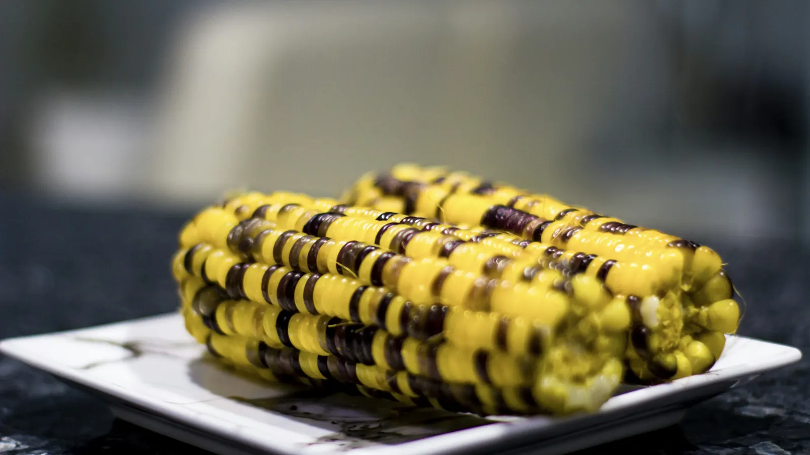 A charred cob of corn dressed with butter and chile on a white plate