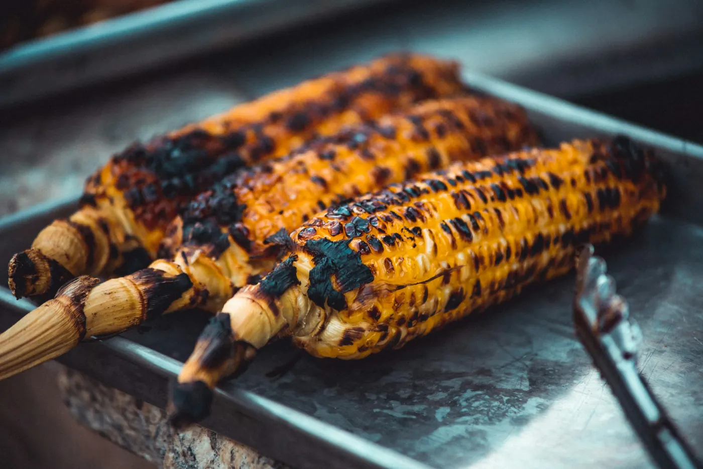 Cobs of blackened corn on skewers over a grill