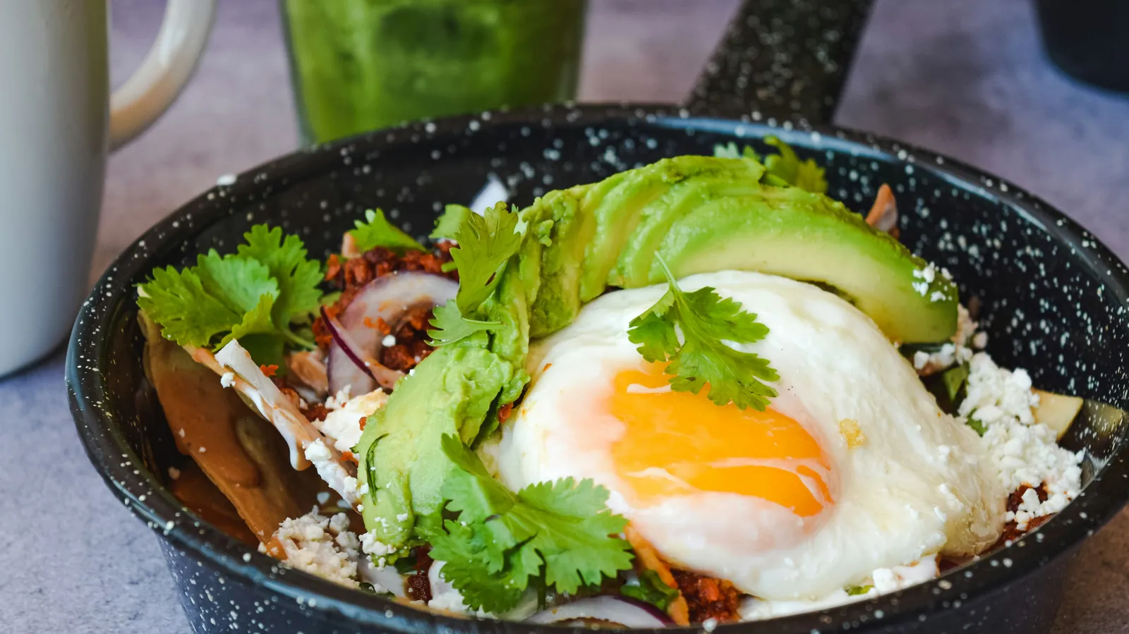 Chilaquiles in a skillet topped with a fried egg, avocado and cilantro