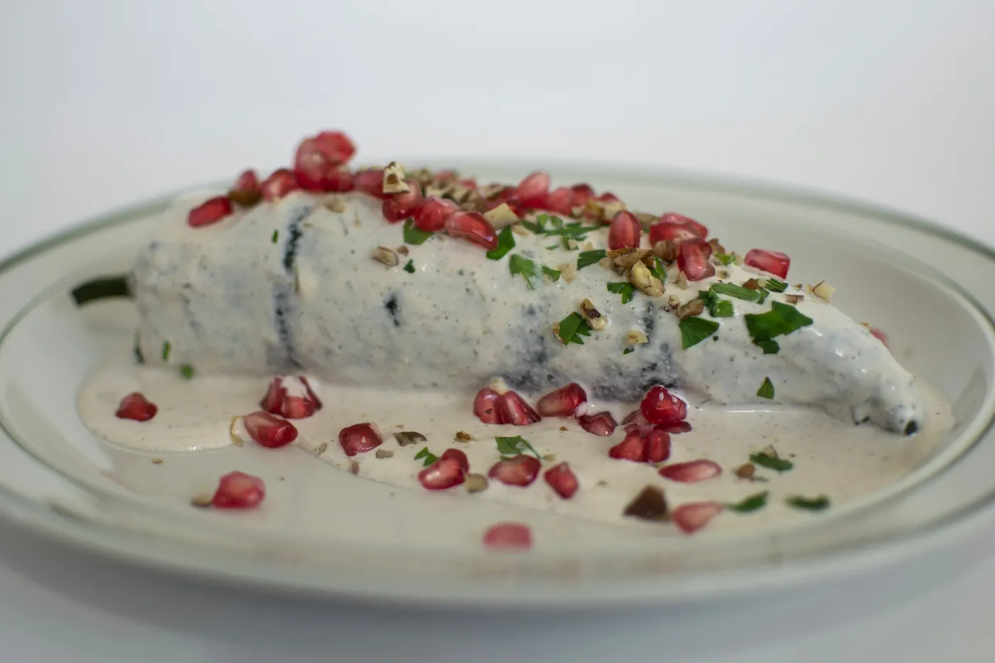 A long stuffed pepper covered in pale sauce and pomegranate on a white plate