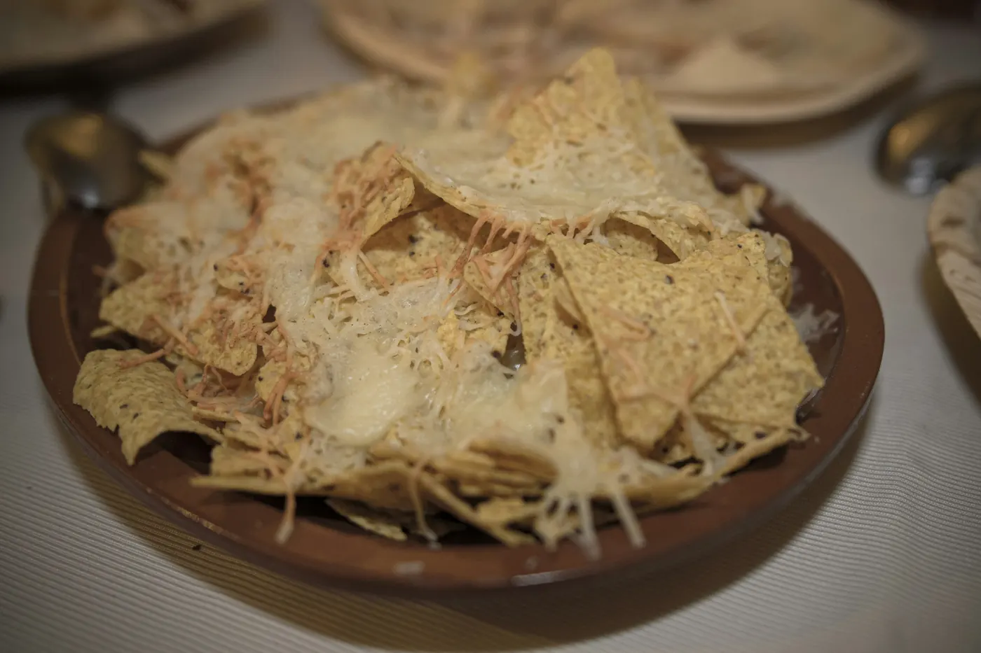 Tortilla chips under melted cheese in a shallow clay dish