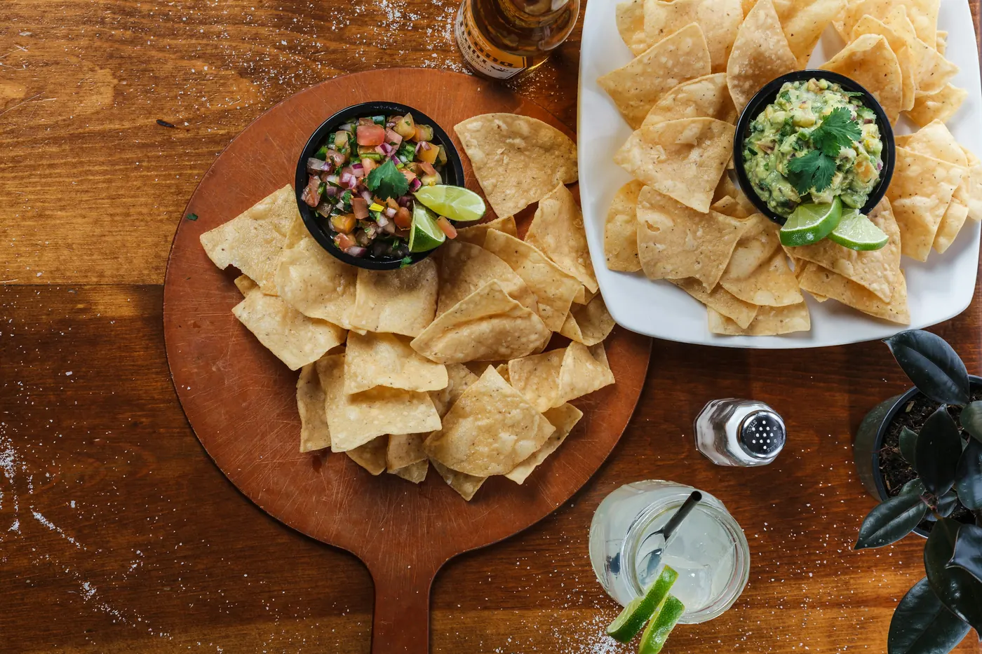 Tortilla chips on a wooden board with two small bowls of dip