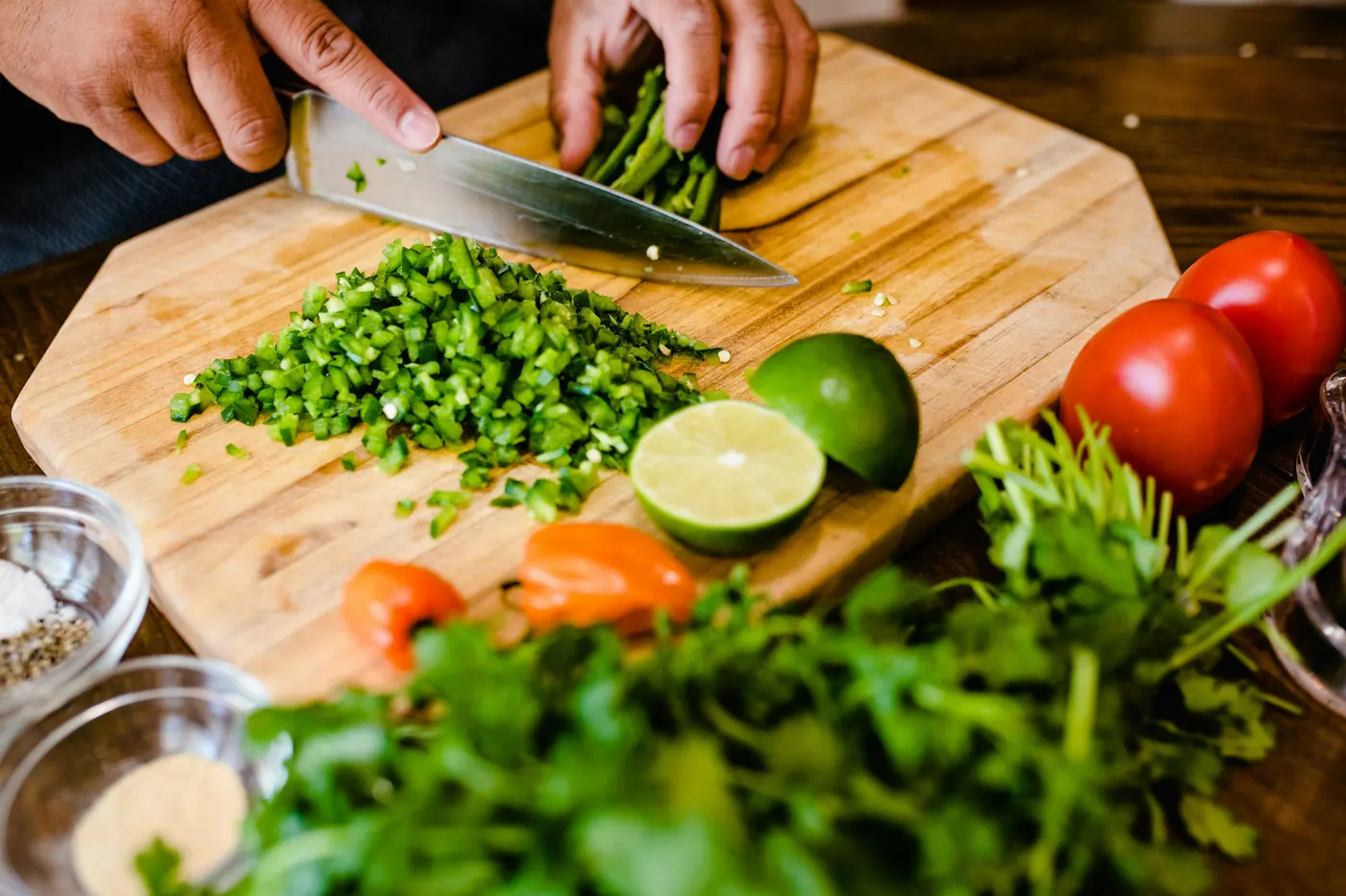 Chopped green chile on a board with lime, tomato and cilantro