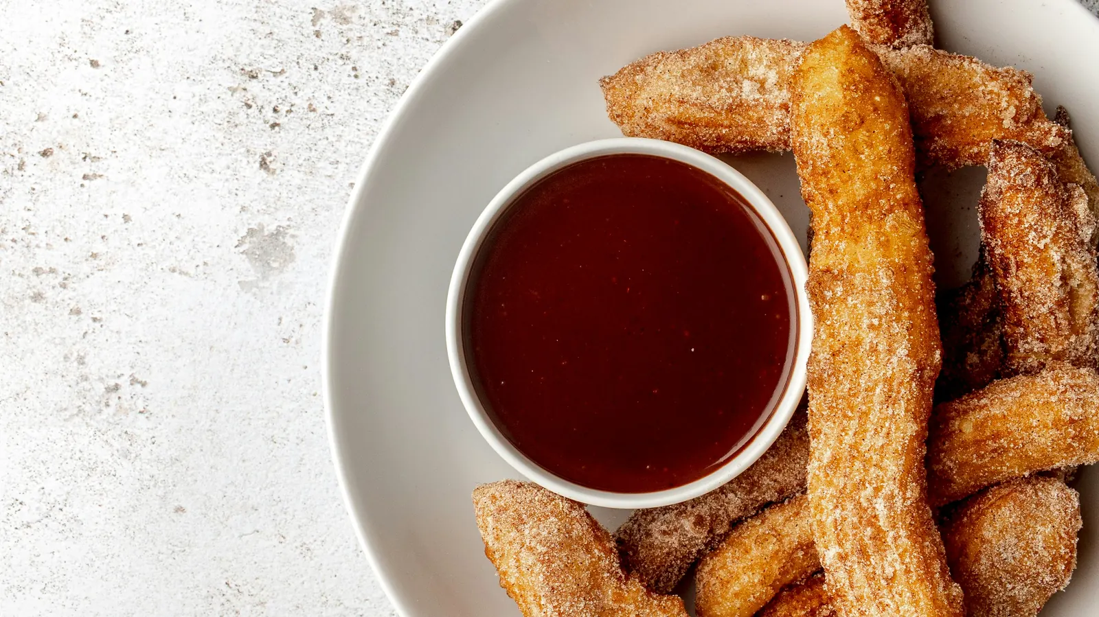 A plate of sugared churros beside a bowl of thick chocolate