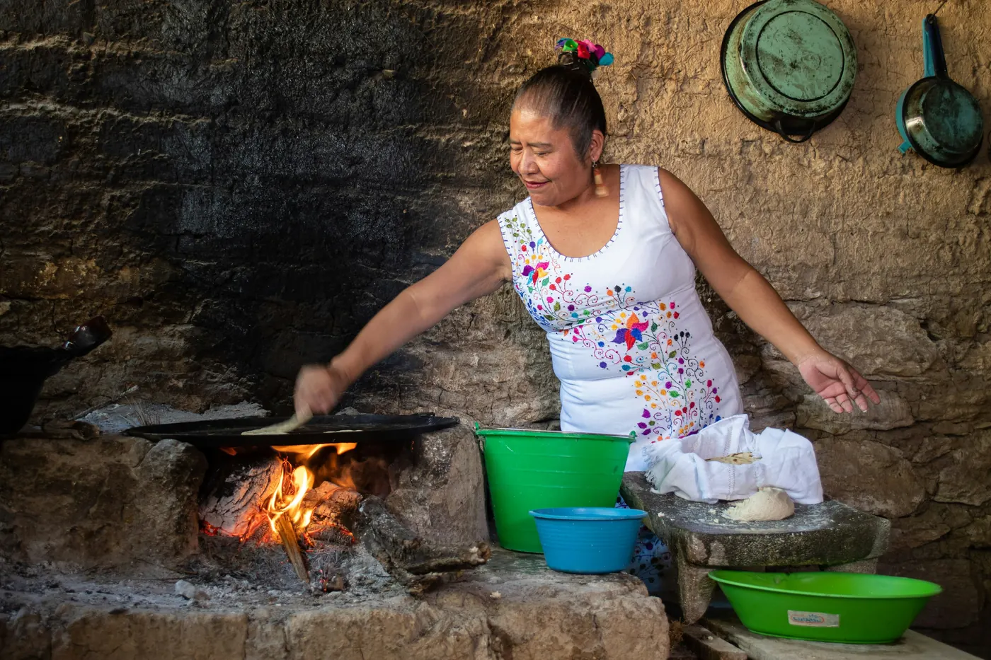 A cook working over an open wood fire with pots alongside
