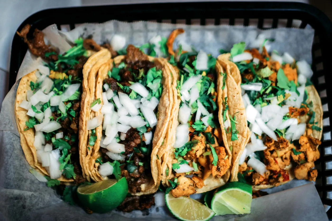 Corn tortilla tacos topped with diced onion, cilantro and lime wedges