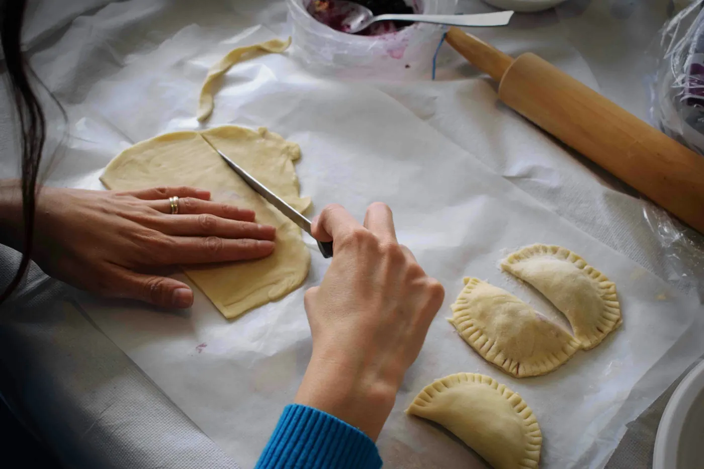Hands crimping and sealing the edge of a filled pastry