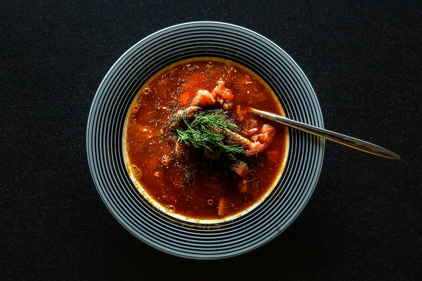 A dark bowl of deep red chile broth with a spoon resting in it