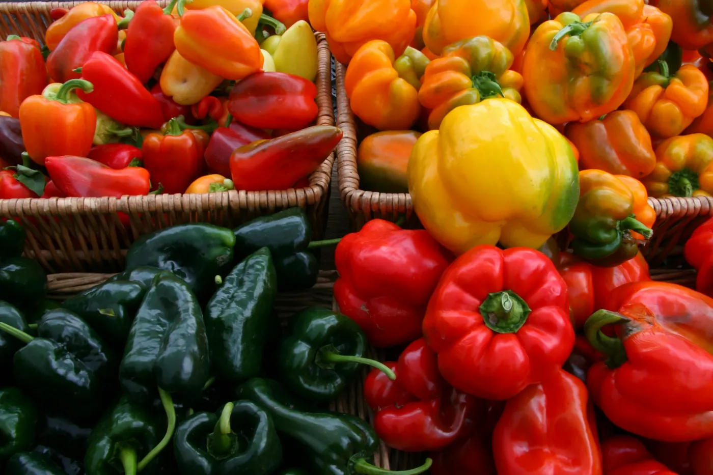 Baskets of dark green, red and yellow peppers at a market