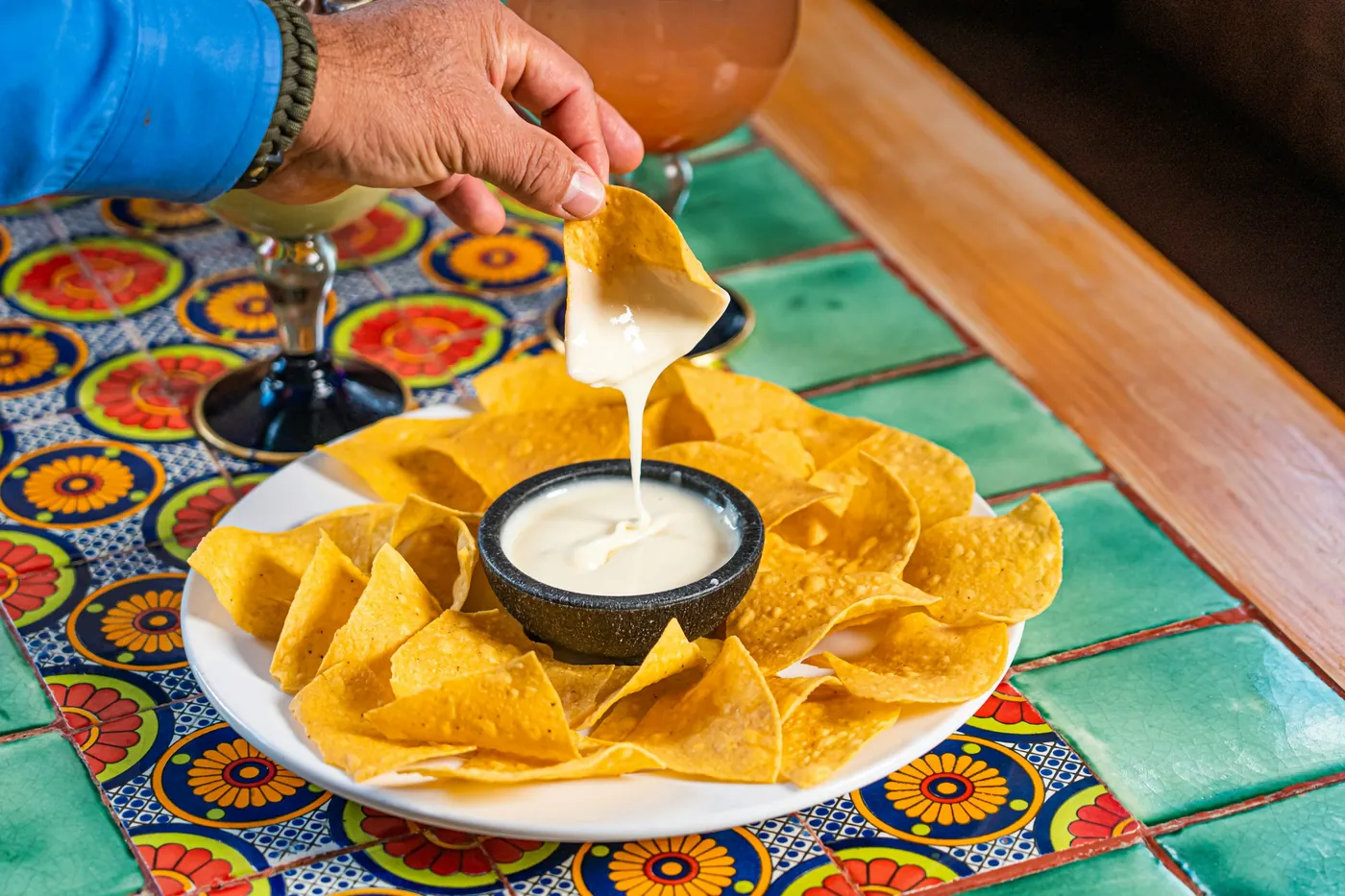 A hand dipping a tortilla chip into a small bowl of white queso