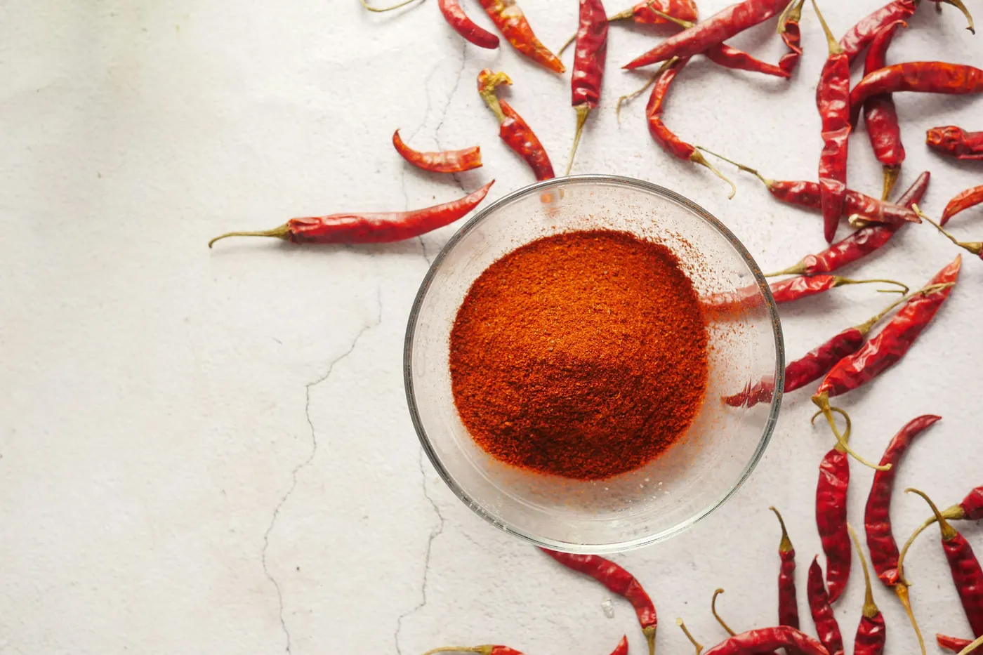 Small dried red chiles scattered around a bowl of ground chile powder
