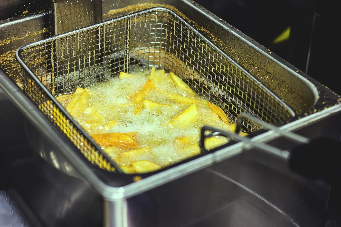 Pale yellow batter cooking in hot oil in a fryer basket
