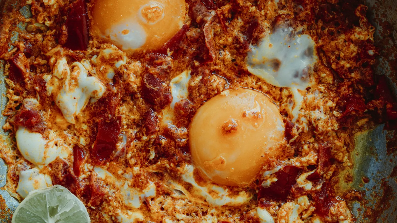 Fried eggs sitting in a red chile sauce with lime alongside