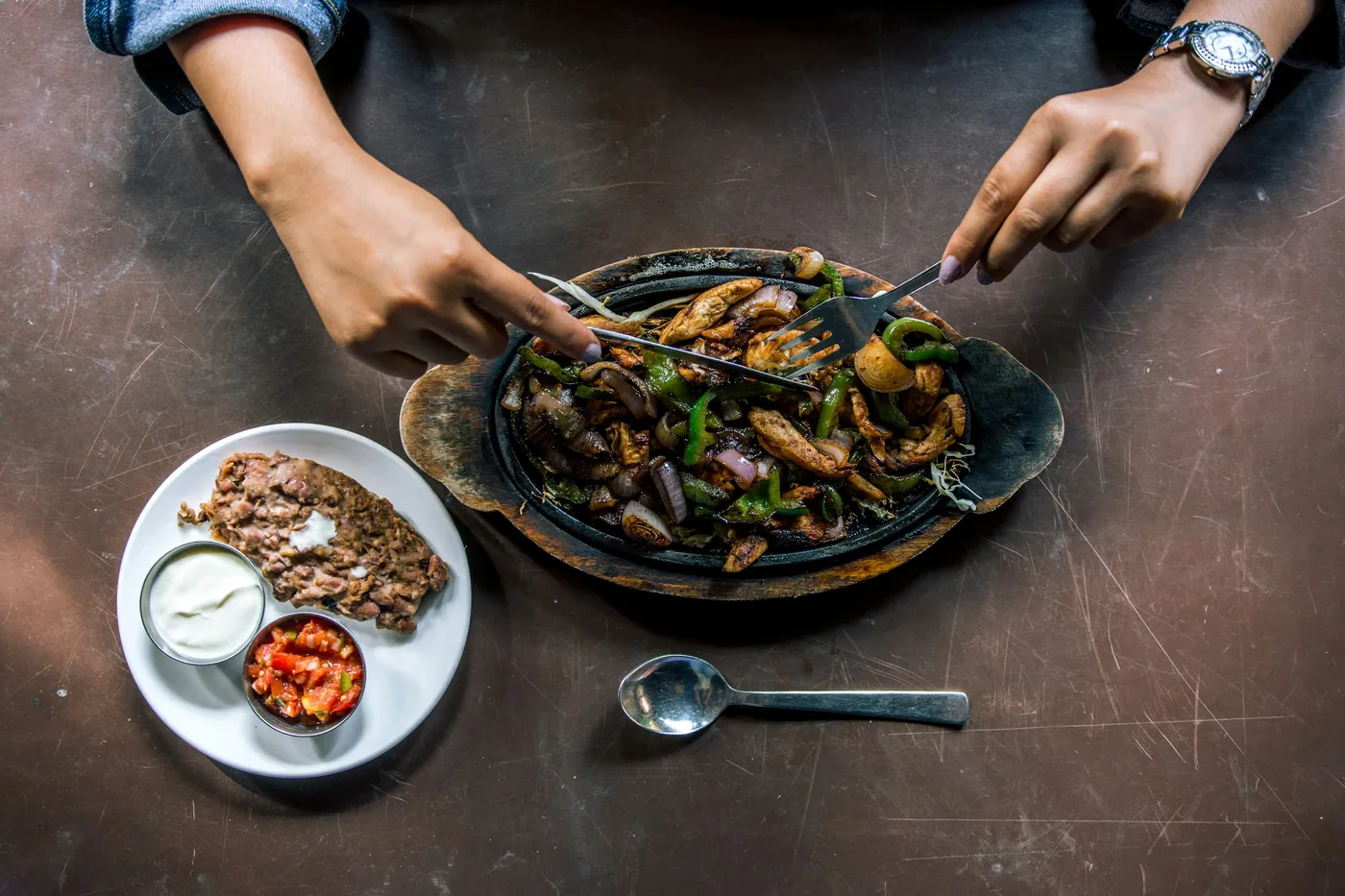 A cast iron fajita skillet on a dark table surrounded by small side dishes