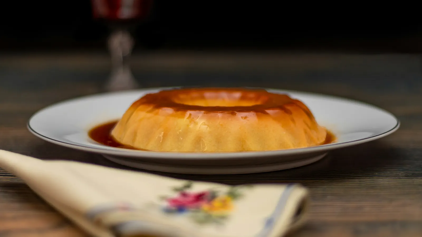 A round flan on a white plate with caramel sauce around it