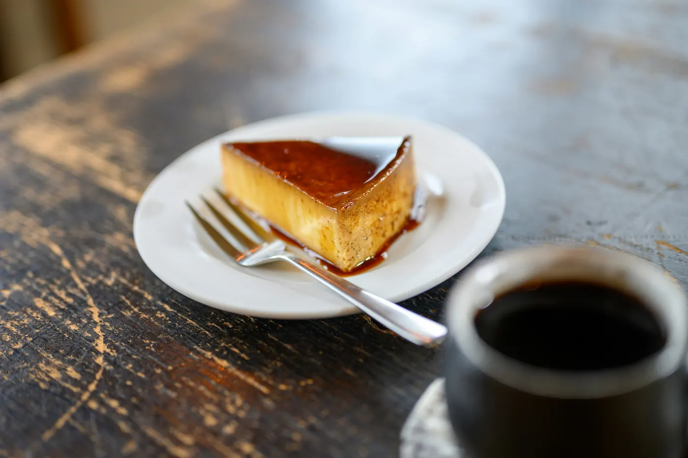 A slice of flan on a plate beside a small cup of black coffee