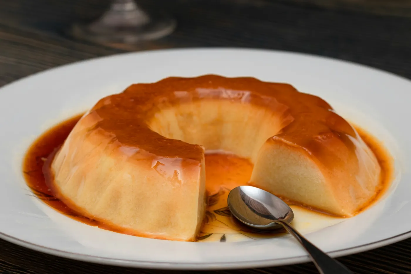 A pale set custard on a white plate with dark caramel pooled around the base