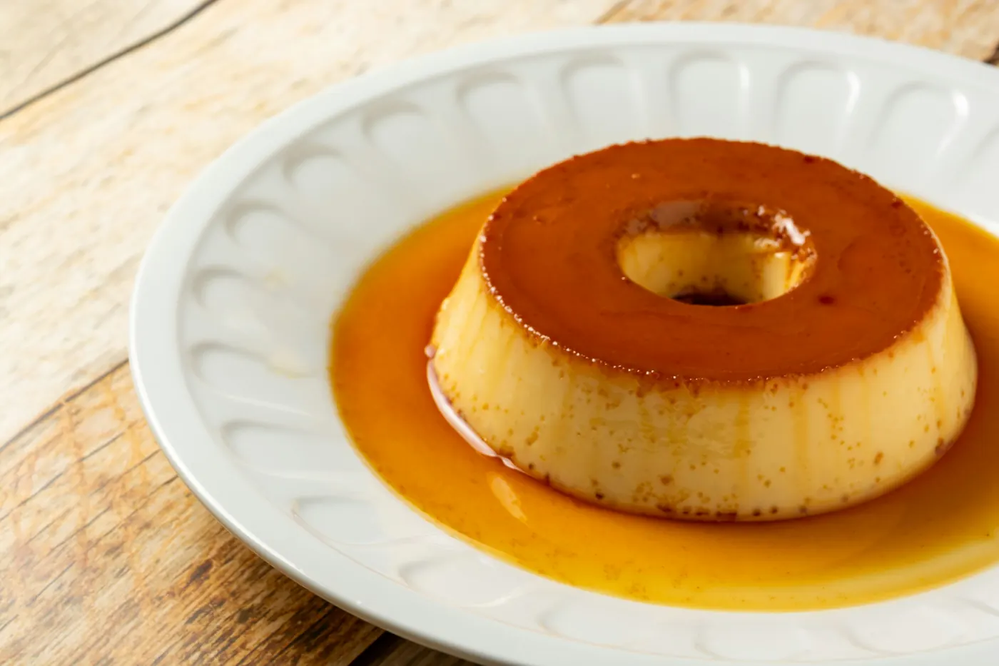 A flan on a plate with caramel sauce pooling around the base