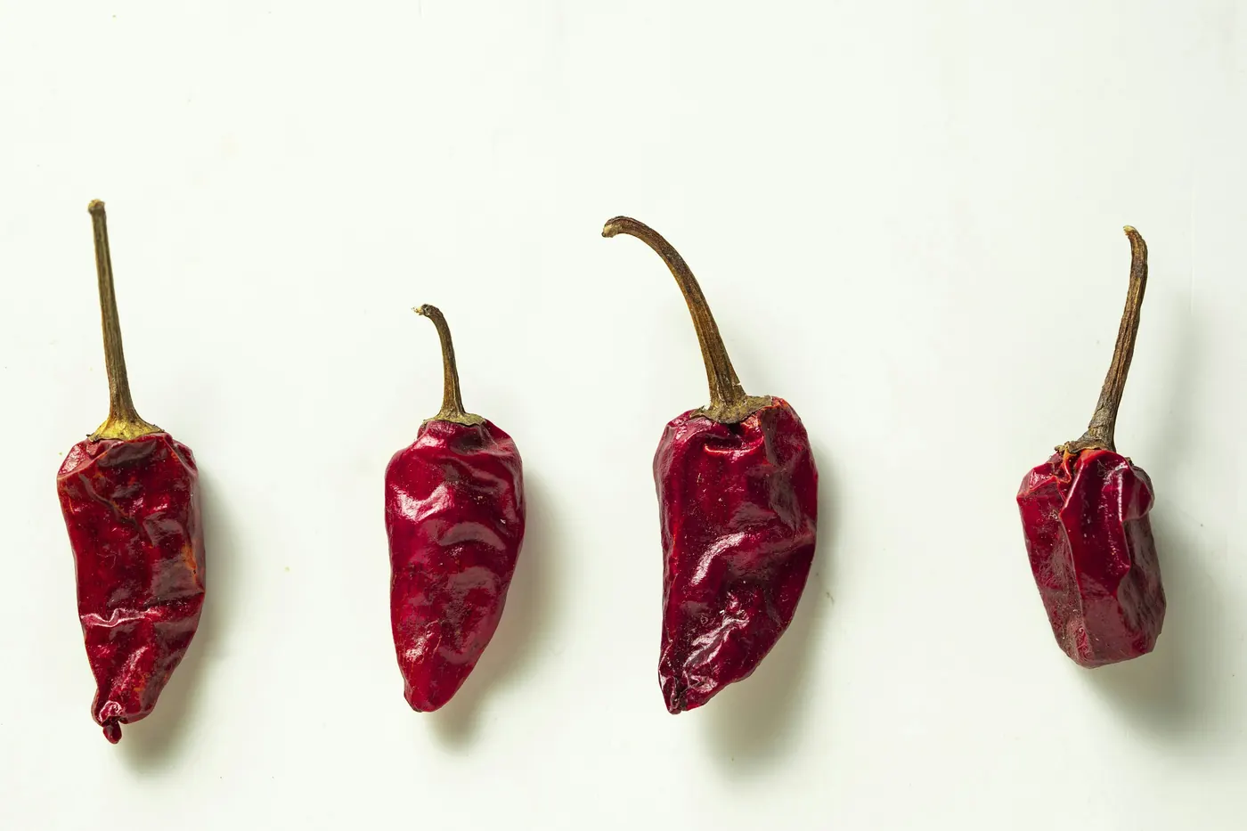Four dried red chile pods arranged on a white background