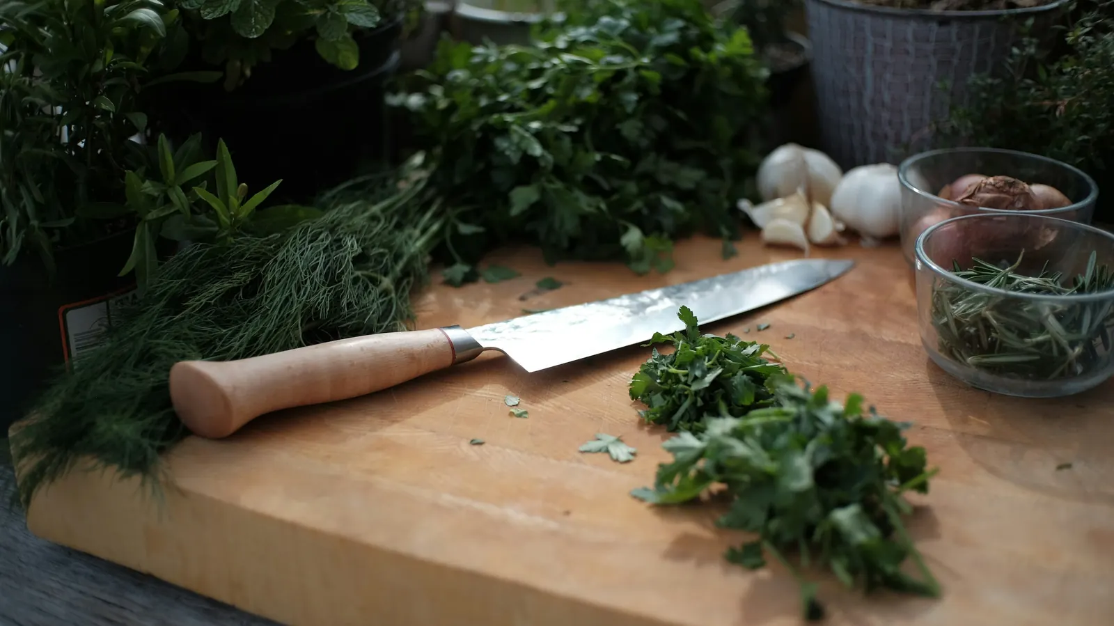 Fresh green herbs on a wooden board beside a knife and garlic