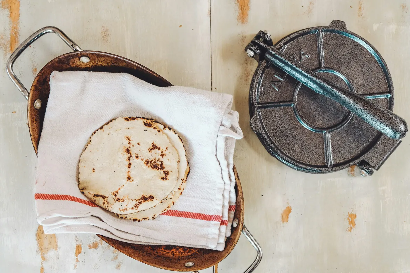 Fresh tortillas wrapped in a cloth beside a metal tortilla press