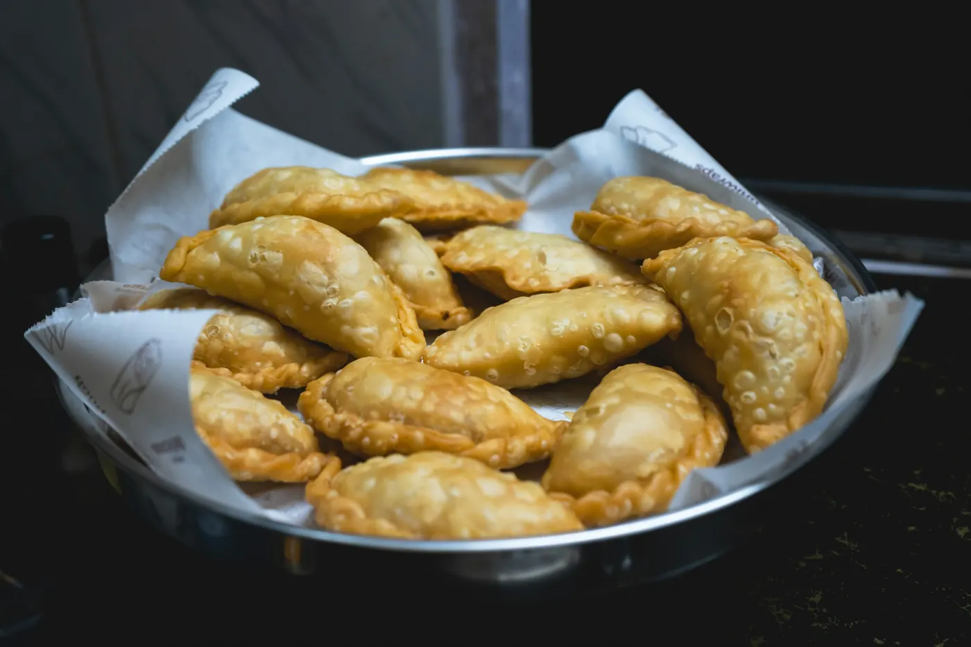Deep-fried empanadas piled in a metal serving basket