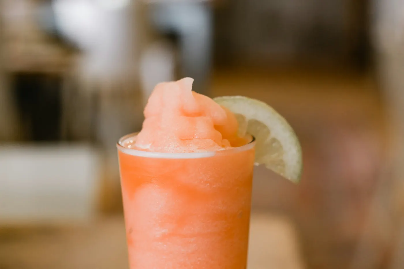 A pale orange frozen margarita served in a cup with a lime wedge