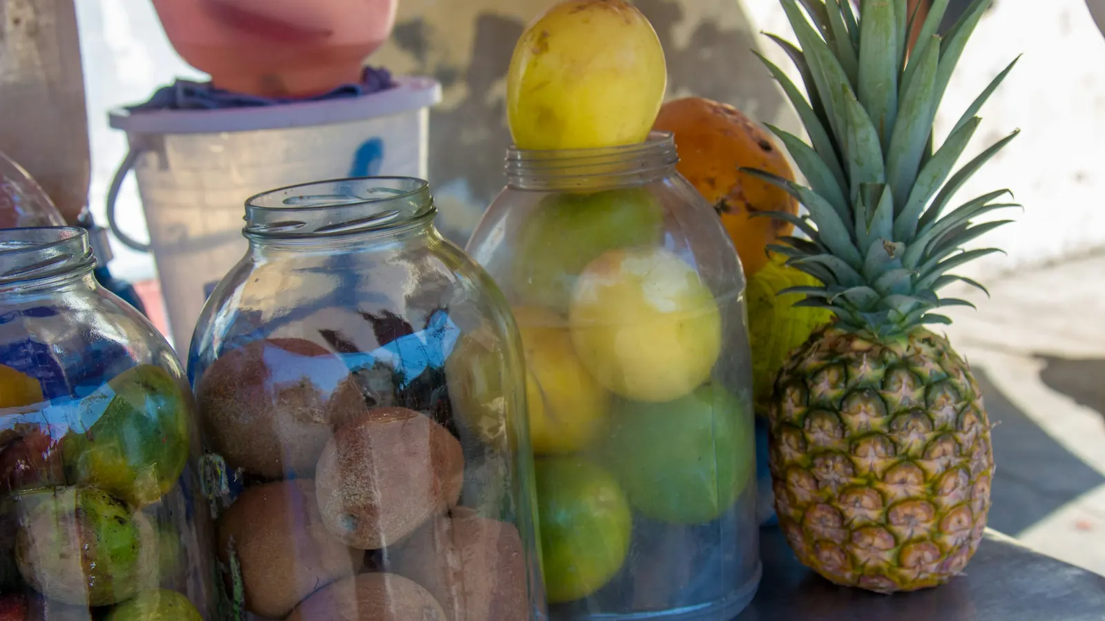 Large glass jars of fruit drinks beside a pineapple at a stall