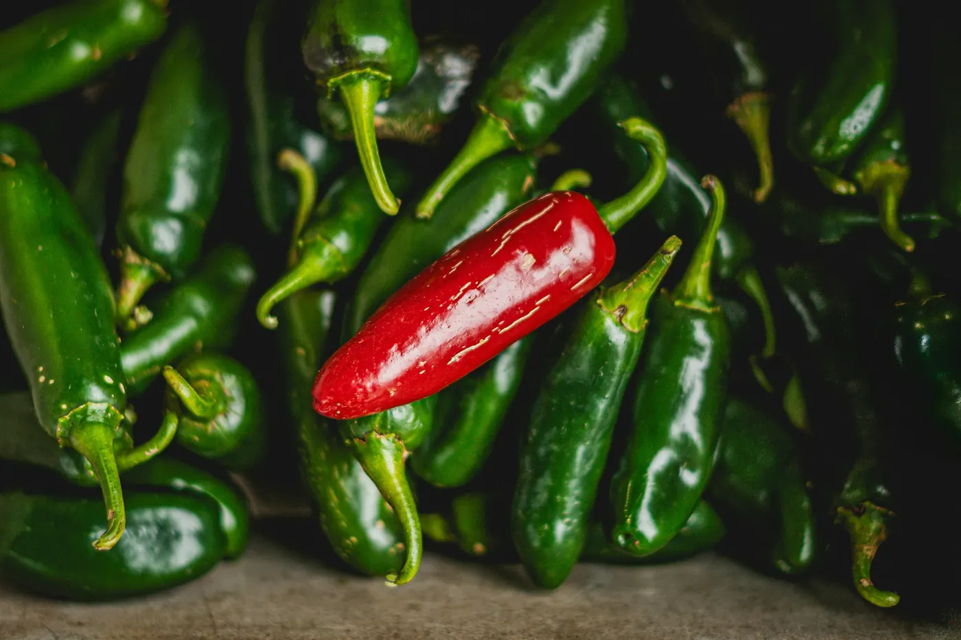 Green jalapeno peppers with a single red ripe one among them