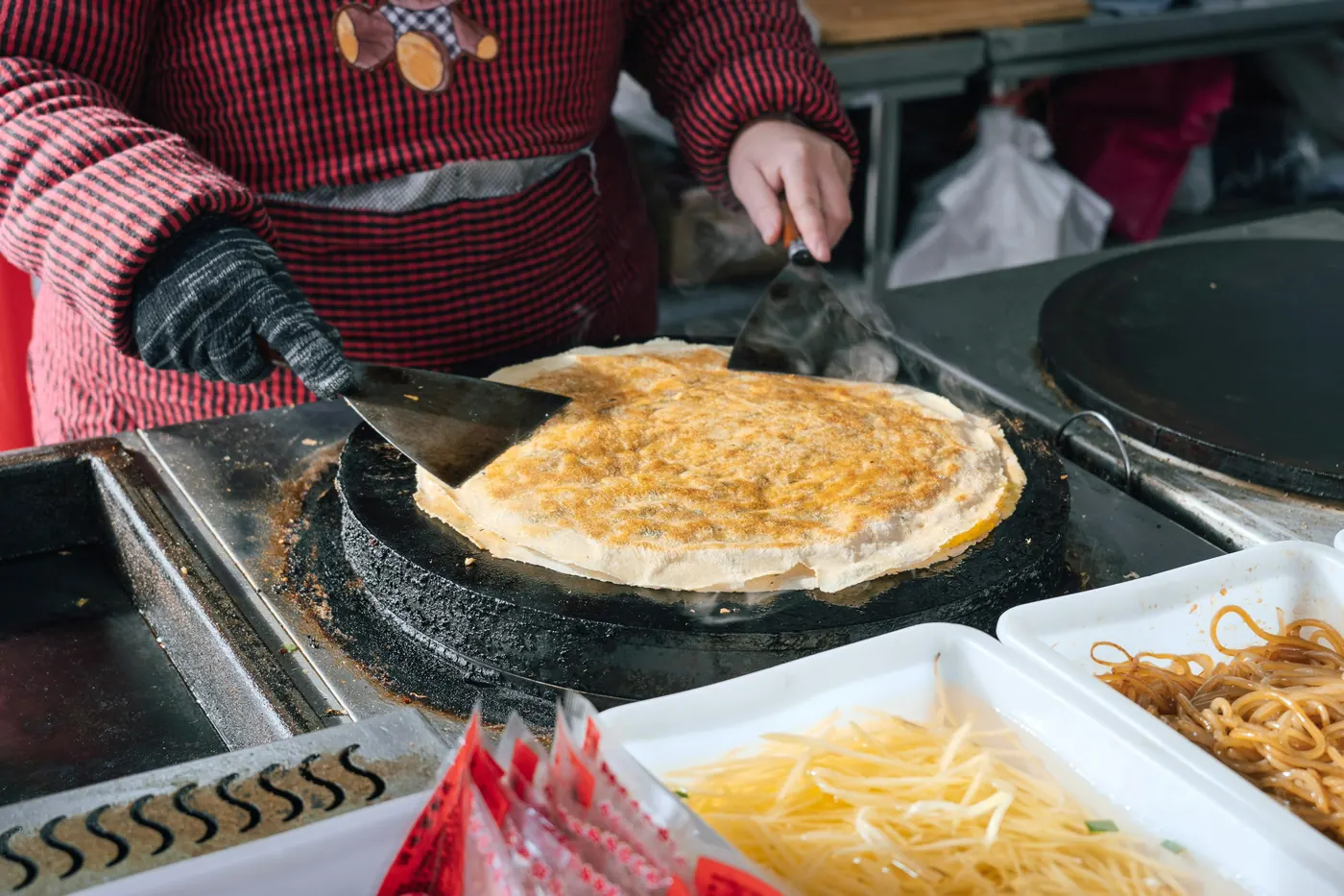A vendor cooking a large folded tortilla on a flat griddle at a stall