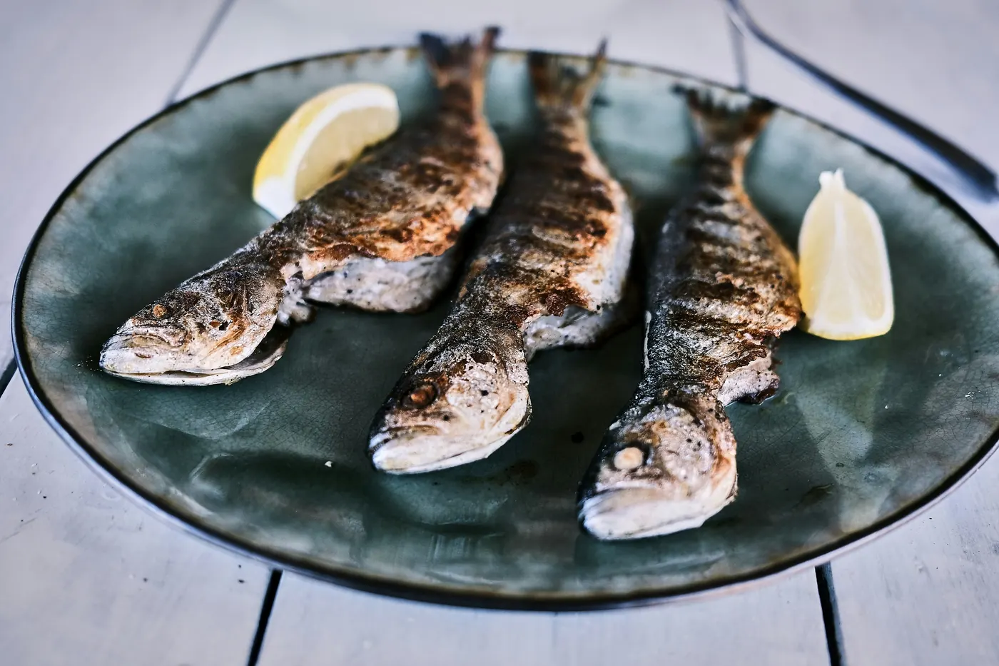 Three grilled fish laid out on a dark platter with lemon