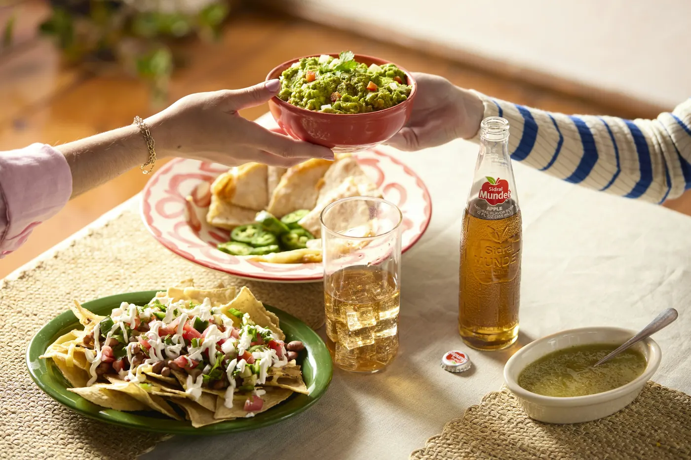 A plate of tacos being passed across a table with a drink alongside