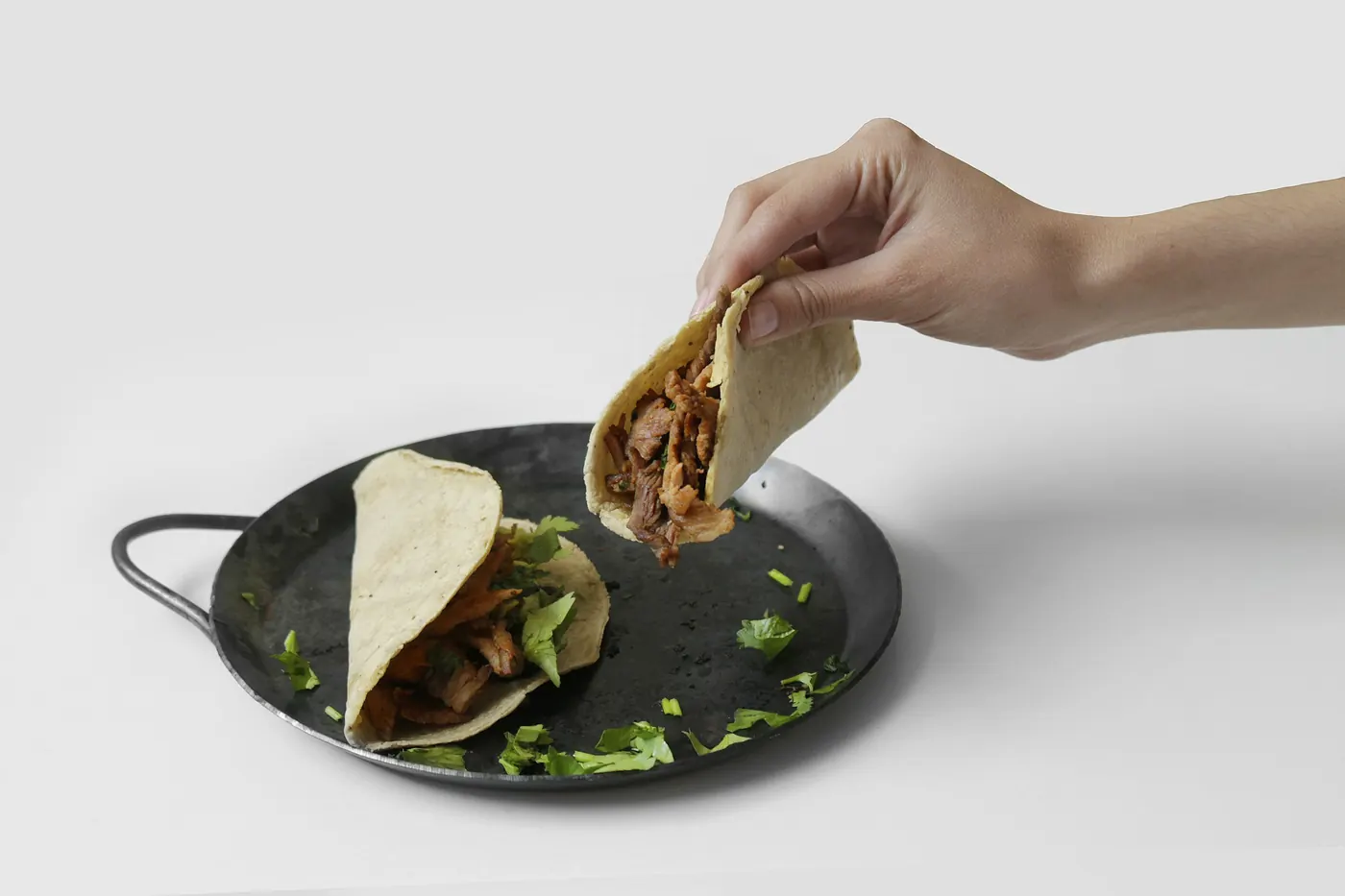 A hand lifting a folded filled tortilla out of a shallow pan