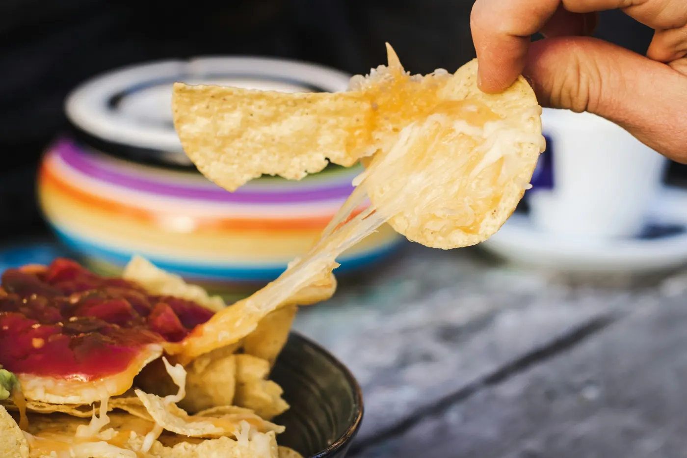 A hand lifting a tortilla chip out of a bowl of chips