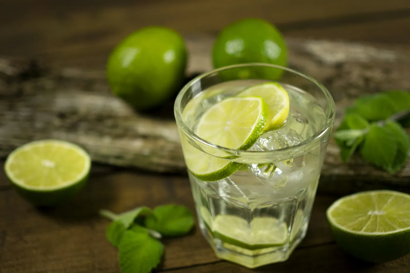 A simple lime drink in a glass on a wooden table with fresh limes
