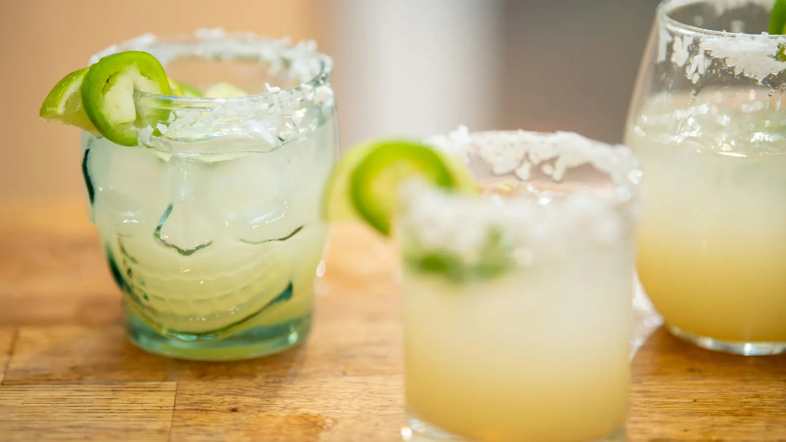 Two margaritas on the rocks with salted rims and lime on a wooden bar