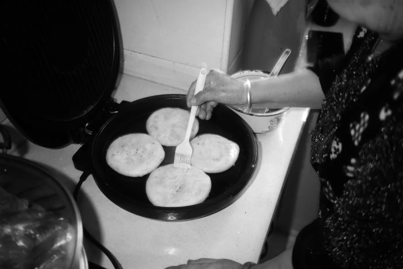 Rounds of masa dough being pressed and cooked on a griddle