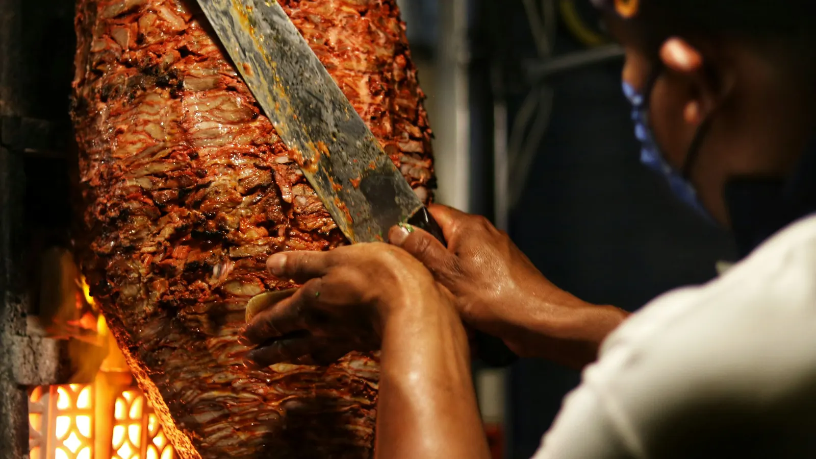 A cook shaving cooked meat from a tall vertical spit