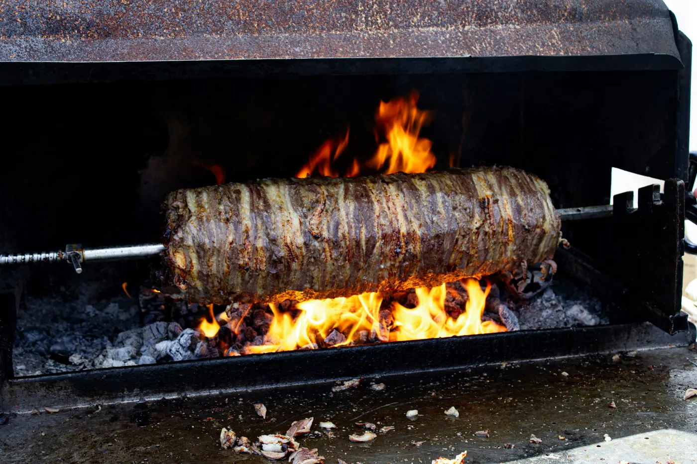 A long spit of meat rotating over an open flame