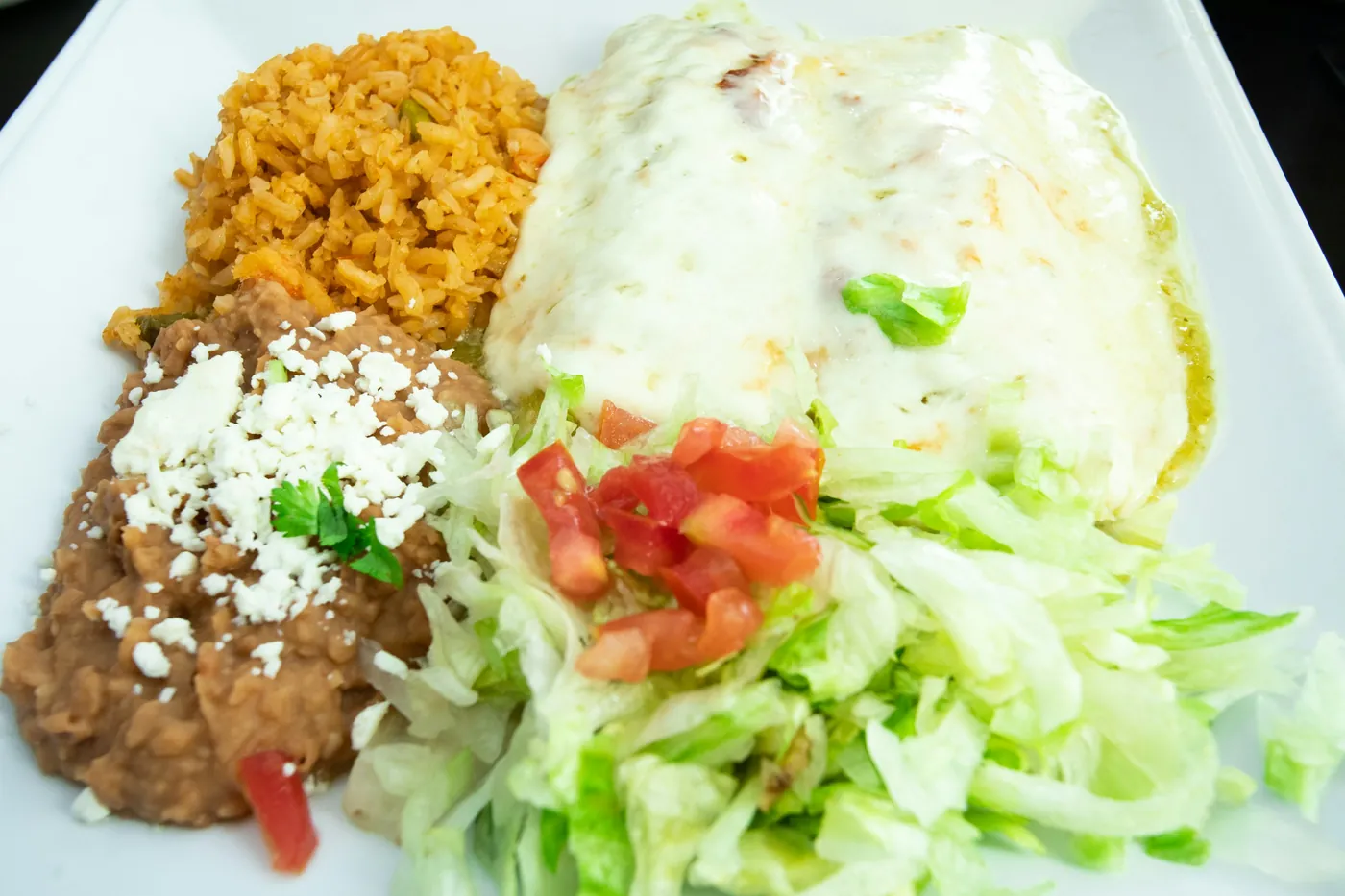 A Mexican combination plate with rice, refried beans, lettuce and pico de gallo