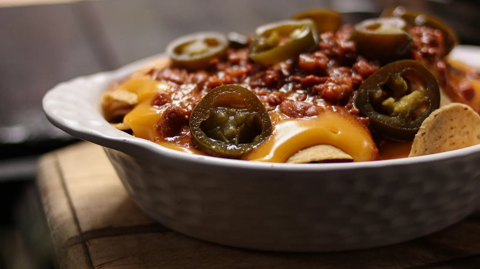 A dish of tortilla chips under melted yellow cheese with sliced jalapenos