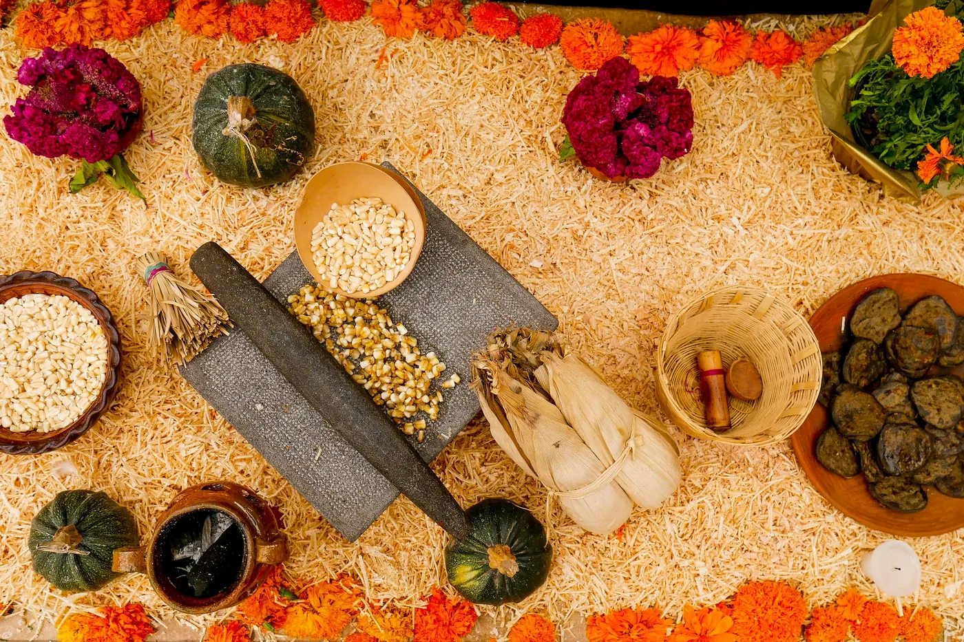Small bowls of seeds, fruit and flowers arranged along a sand-covered altar
