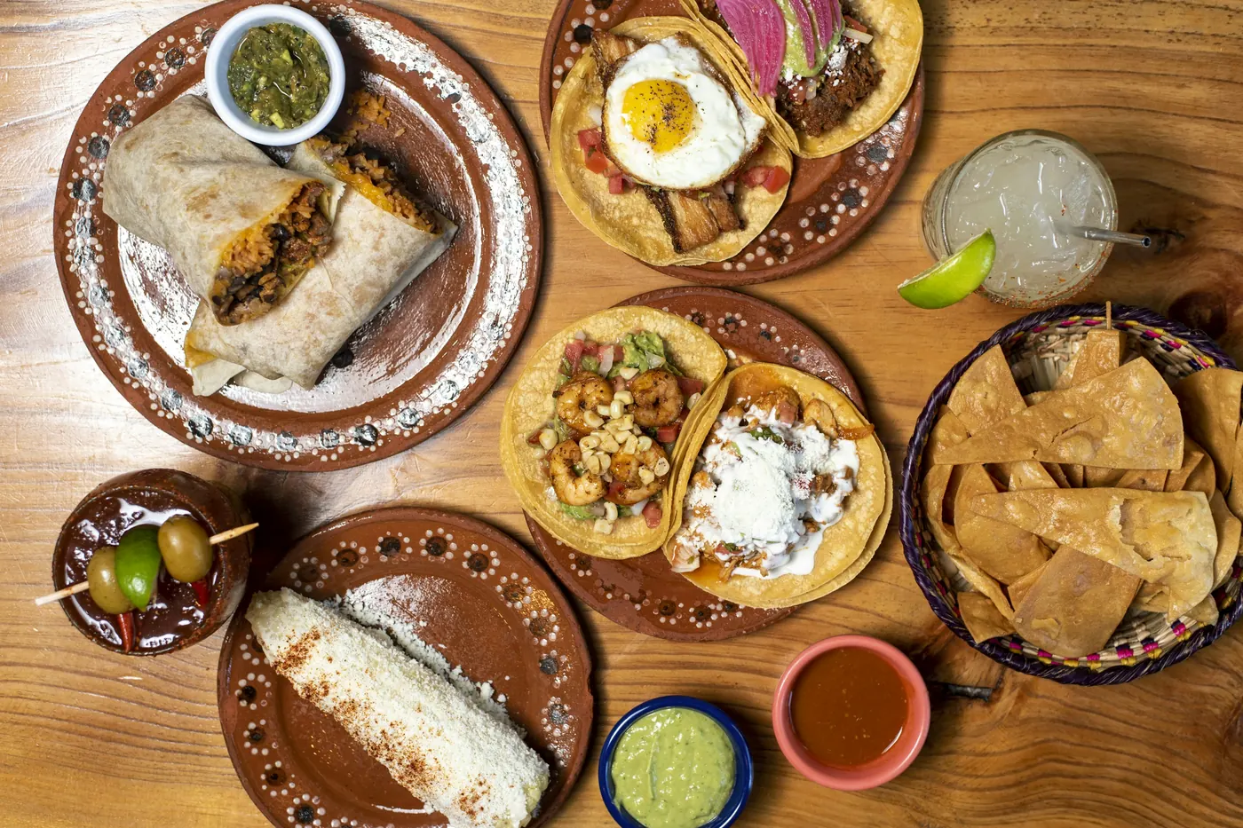 An overhead spread of several Mexican dishes, tortillas and drinks