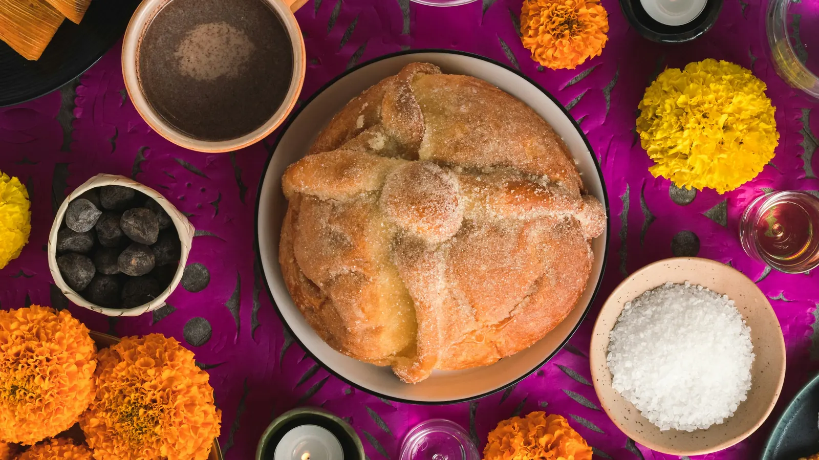 Round sweet bread on a plate surrounded by marigolds and small bowls