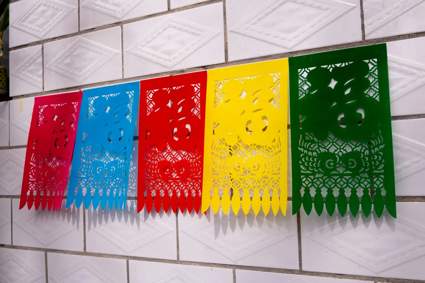 Rows of red, yellow and green cut-paper banners against a white tiled wall